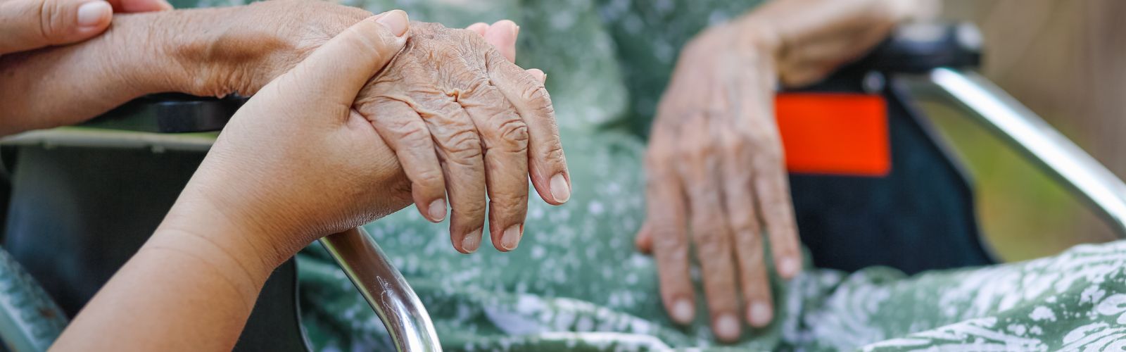Junge Hand hält die Hand einer alten Frau im Rollstuhl