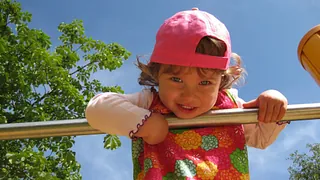 Kleines Mädchen hält sich an einer Stange fest und lächelt