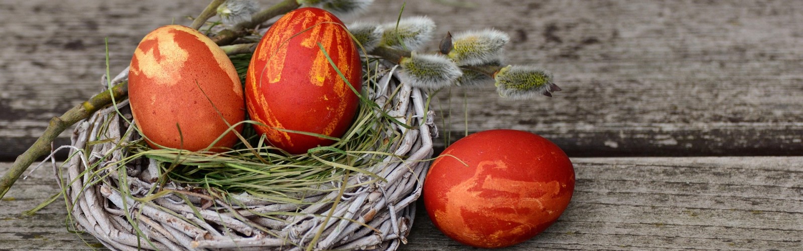 Drei bemalte Ostereier, davon zwei in einem Strohnest