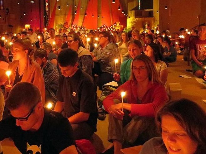 Viele Menschen beten in einer Kirche in Taizé im Kerzenschein