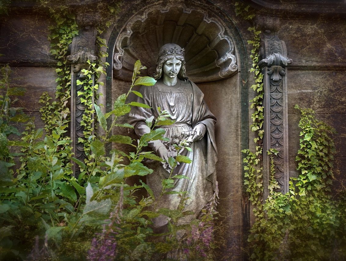 Engelsstatue auf einem Friedhof, von Efeu und Pflanzen umgeben