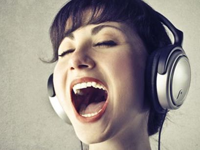 Frau mit Kopfhörern singt begeistert mit geschlossenen Augen