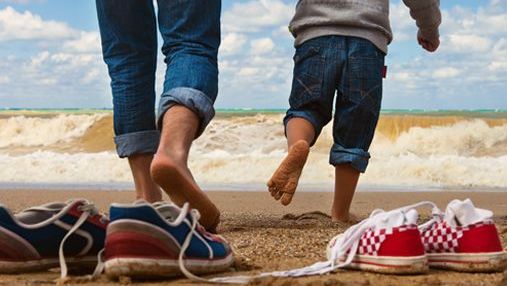 Erwachsener und Kind barfuß am Strand, Schuhe im Sand