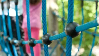 Kind klettert auf einem blauen Kletternetz im Freien