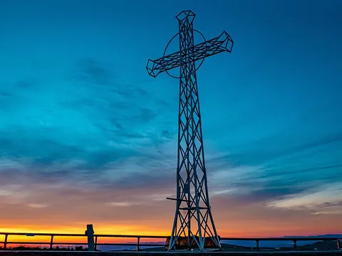 Metallkreuz auf Berg vor farbigem Sonnenuntergang