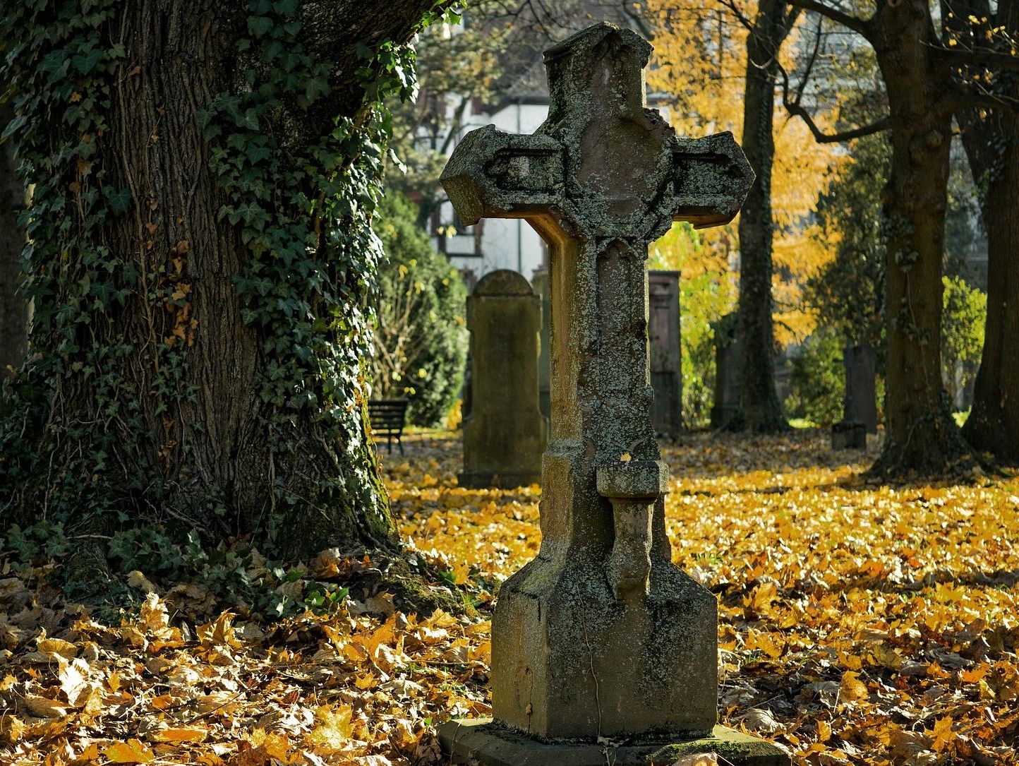 Moosbewachsenes Steinkreuz auf herbstlichem Friedhof